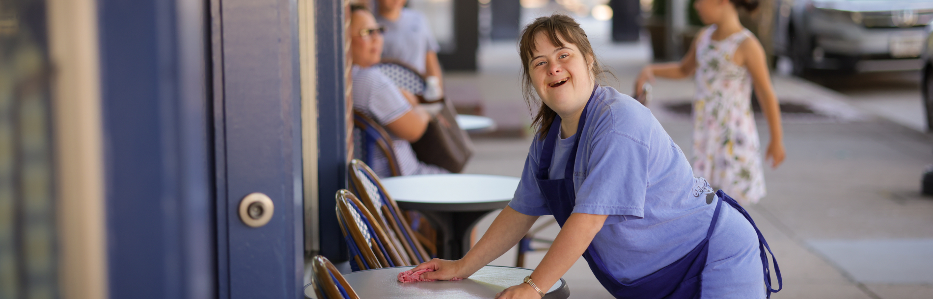 A woman supported by Penn-Mar cleaning a table outside at her cafe job.